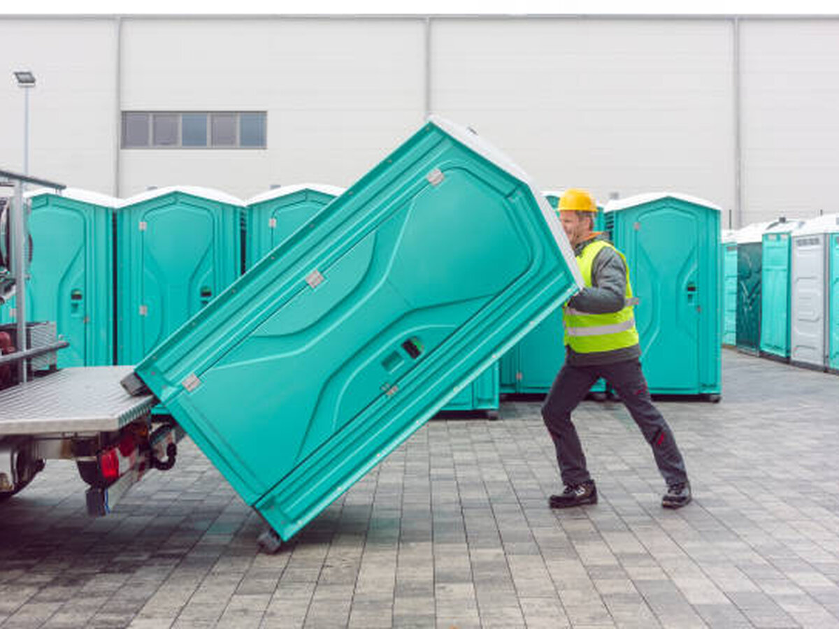 Delivery crew member unloading a portable restroom unit from a truck